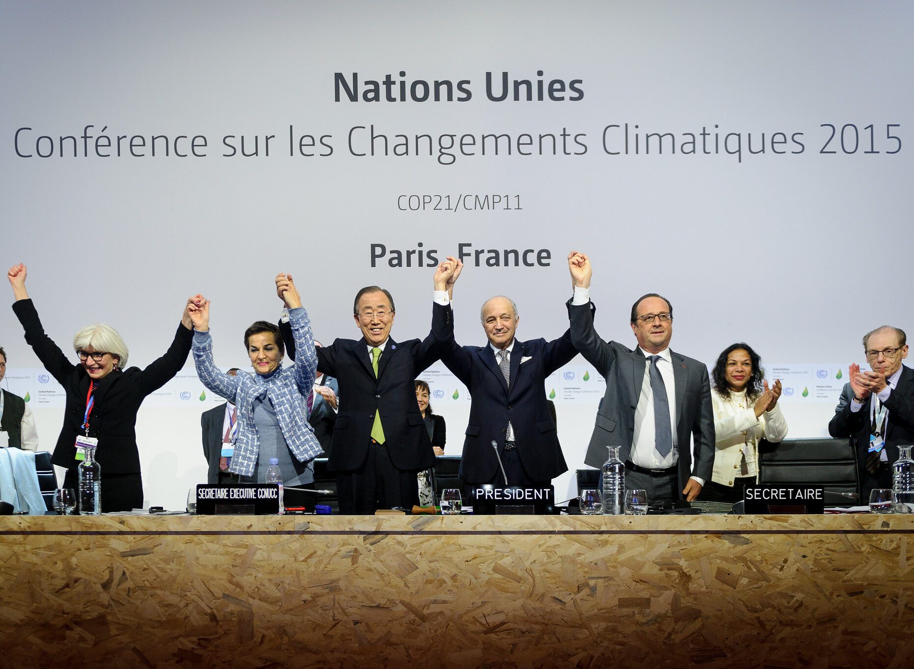 Five leaders smiling hand in hand with arms raised at the United Nation's COP21 in 2015.