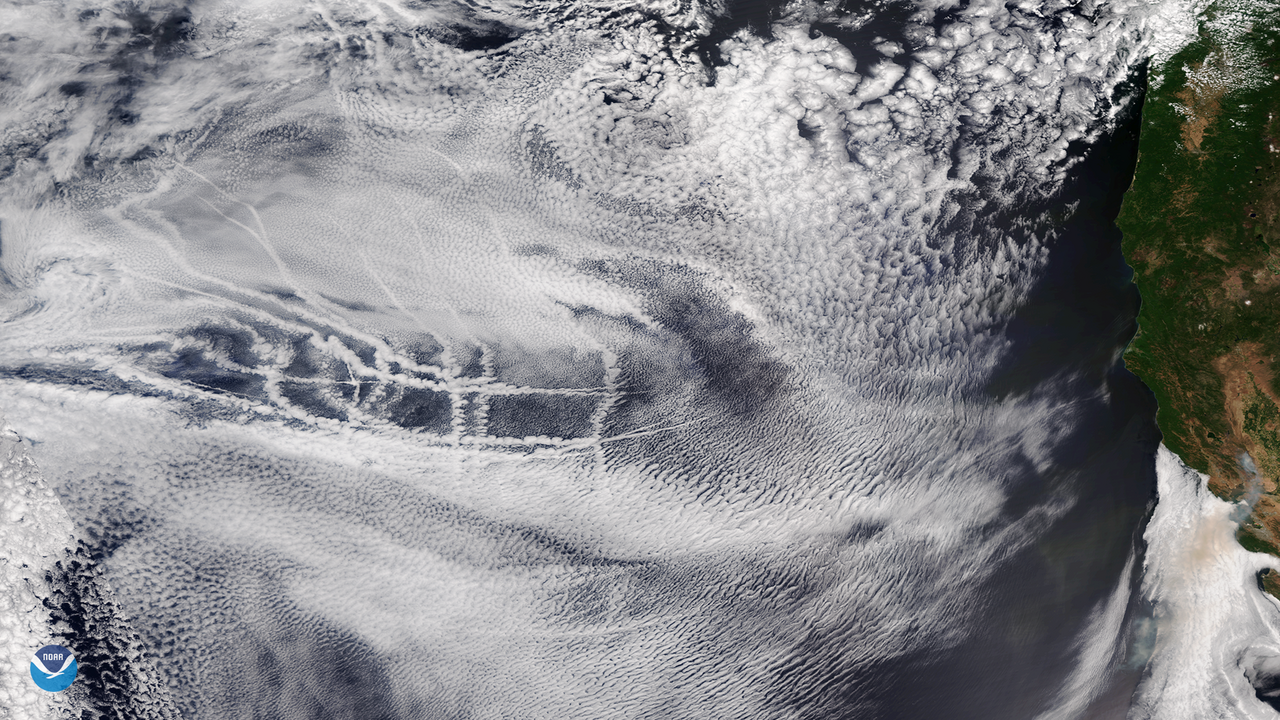 Satellite view of ripply white clouds overlying the ocean with some streaks steaks of white clouds shown across them.